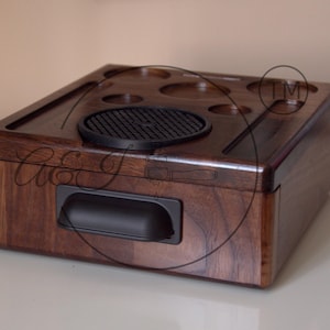 May include: A dark brown wooden box with a black handle and a black rubber mat with a grid pattern. The box has several circular indentations on the top.