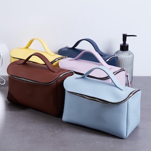 Peut inclure: Une collection de cinq trousses de toilette rectangulaires avec poignées supérieures et fermetures éclair argentées. Les trousses sont disponibles en couleurs unies dont marron, bleu clair, jaune, bleu foncé et rose clair, au design structuré.