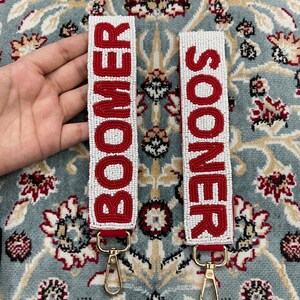 May include: Two white beaded keychains with red lettering. The keychain on the left says "BOOMER" and the keychain on the right says "SOONER".