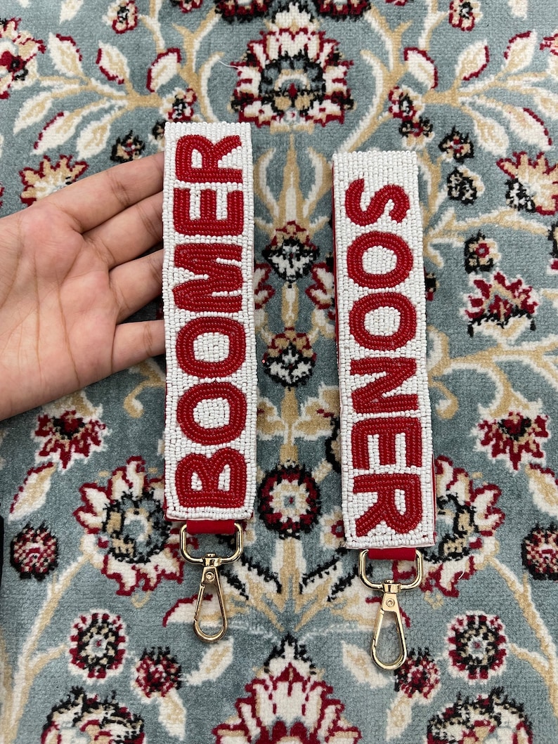 May include: Two white beaded keychains with red lettering. The keychain on the left says "BOOMER" and the keychain on the right says "SOONER".