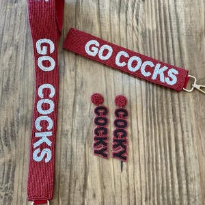 May include: A set of red beaded jewellery featuring the words "Go Cocks" and "Cocky". The set includes a lanyard, a keychain, and a pair of earrings.