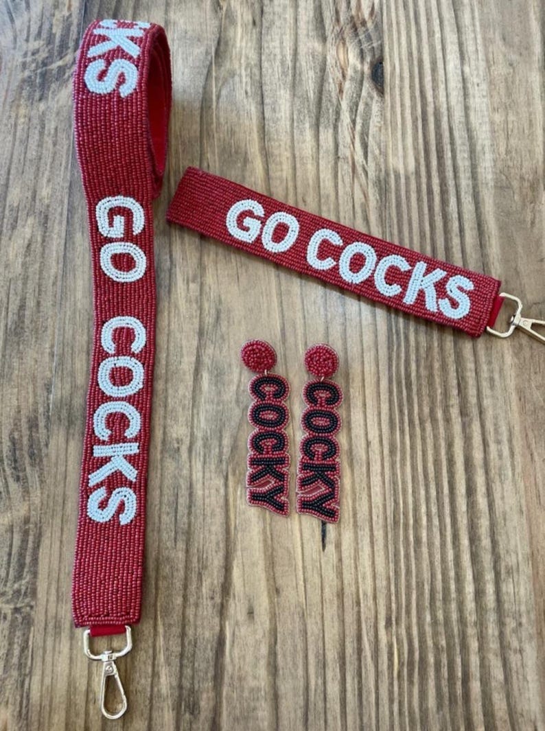 May include: A set of red beaded jewellery featuring the words "Go Cocks" and "Cocky". The set includes a lanyard, a keychain, and a pair of earrings.
