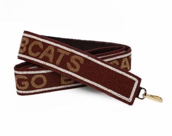 May include: A brown beaded strap with gold lettering that reads "GO BCATS". The strap has a gold metal clasp.