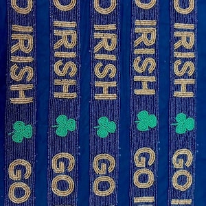 Puede incluir: Cinco tiras de cuentas con las palabras "GO IRISH" en cuentas doradas sobre un fondo azul oscuro. Cada tira tiene un tr&eacute;bol verde.
