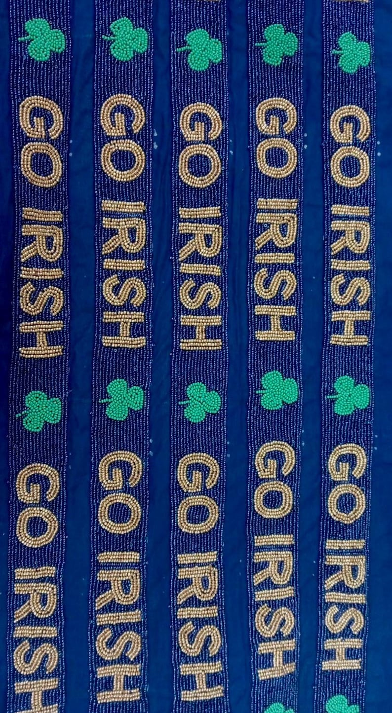 Puede incluir: Cinco tiras de cuentas con las palabras "GO IRISH" en cuentas doradas sobre un fondo azul oscuro. Cada tira tiene un tr&eacute;bol verde.