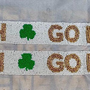 Puede incluir: Pancarta blanca de cuentas con las palabras "Go Irish" repetidas dos veces, con un tr&eacute;bol verde entre cada frase.