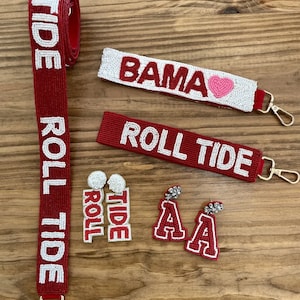 May include: Red and white beaded keychain with the words "Roll Tide" and a small pink heart. There is also a red and white beaded strap with the words "Roll Tide" and a pair of red and white beaded earrings with the letter "A" and a small rhinestone.