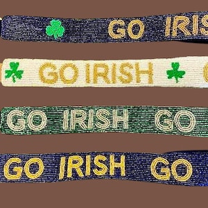 May include: Four beaded keychains with gold and white lettering that reads "GO IRISH" and green shamrock accents. The keychains are in blue, white, green, and blue.