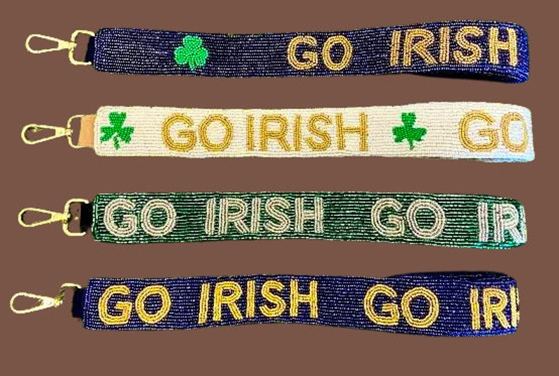 Puede incluir: Cuatro llaveros de cuentas con letras doradas y blancas que dicen "GO IRISH" y detalles de tr&eacute;bol verde. Los llaveros son de color azul, blanco, verde y azul.