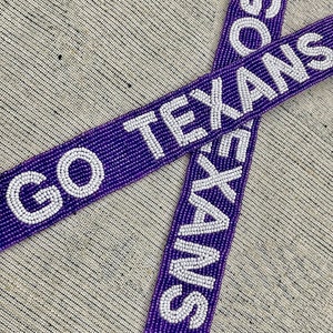 May include: Two purple beaded straps with white beads spelling out "GO TEXANS" and "TEXANS".