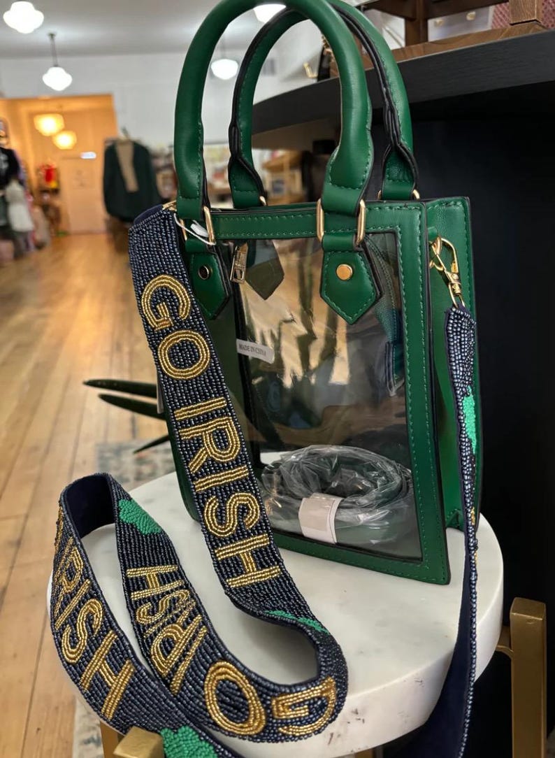 Puede incluir: Un bolso de mano verde y transparente con una correa de cuentas doradas que dice "Go Irish".