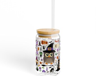 May include: A clear glass drinking cup with a wooden lid and a straw. The cup is decorated with Halloween-themed illustrations, including an owl wearing a witch hat, pumpkins, and a black cat. The cup is designed for cold beverages.