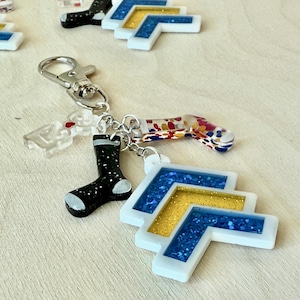 May include: A white and blue glitter chevron charm with a black and white glitter sock charm, a red and white glitter sock charm, and a silver key chain.