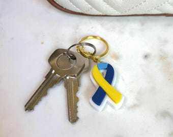 May include: A gold key chain with a blue and yellow ribbon charm. The ribbon is a symbol of awareness for autism.