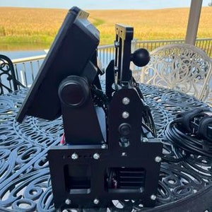 K&ouml;nnte beinhalten: Eine schwarze Metallhalterung mit einem gro&szlig;en Bildschirm daran. Die Halterung hat einen Knopf zum Einstellen des Bildschirmwinkels und ein Kugelgelenk zum Schwenken. Der Bildschirm ist mit einem schwarzen Kabel verbunden.