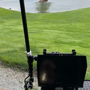 K&ouml;nnte beinhalten: Ein schwarzer und gr&uuml;ner Fischfinder, der an einer schwarzen Stange mit einem wei&szlig;en Griff befestigt ist. Der Fischfinder hat einen schwarzen Bildschirm mit dem Wort "GARMIN" darauf. Der Fischfinder ist auf einem schwarzen St&auml;nder mit den Worten "AMPED OUTDOORS" montiert.