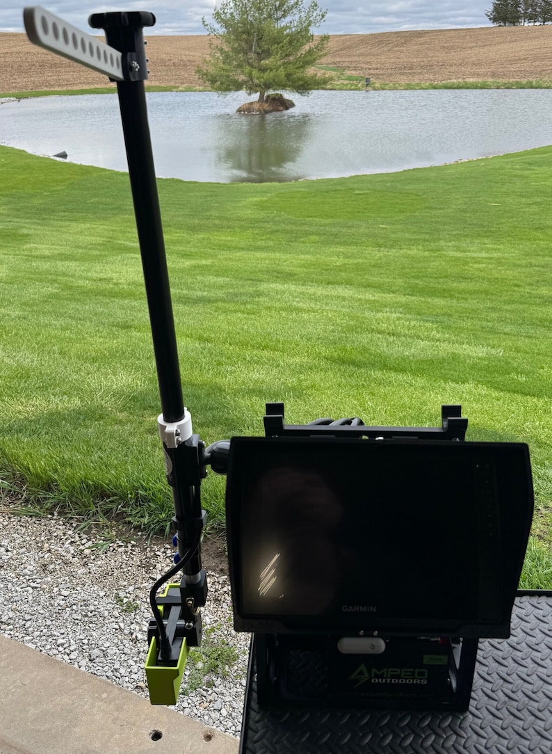 K&ouml;nnte beinhalten: Ein schwarzer und gr&uuml;ner Fischfinder, der an einer schwarzen Stange mit einem wei&szlig;en Griff befestigt ist. Der Fischfinder hat einen schwarzen Bildschirm mit dem Wort "GARMIN" darauf. Der Fischfinder ist auf einem schwarzen St&auml;nder mit den Worten "AMPED OUTDOORS" montiert.