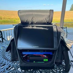K&ouml;nnte beinhalten: Eine schwarze Tragetasche mit einem Rei&szlig;verschluss oben, die einen Garmin-Fischfinder mit einem schwarzen Bildschirm und einen blau-gr&uuml;nen Akku enth&auml;lt.