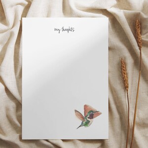 May include: A white notepad with the text "my thoughts" written in black ink. A watercolor illustration of a hummingbird in flight is in the bottom right corner.