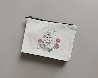 May include: A white canvas zippered pouch with a floral design and the text "You are loved, seen, chosen, worthy, enough".