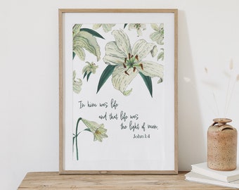 May include: A white framed print with a floral design of white lilies and green leaves. The print features a bible verse: "In him was life and that life was the light of men. John 1:4"