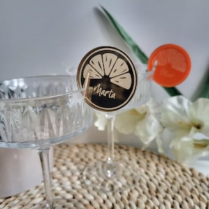 May include: Two clear glass champagne flutes with wooden drink markers. The markers are shaped like a lemon slice and have the name "Marta" written on them.
