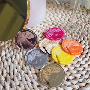 May include: Set of 7 lemon-shaped acrylic drink markers with gold, silver, pink, orange, and yellow accents. Each marker has a different name engraved on it: Trevor, Christie, Oliver, Richard, Stephanie, and Agata.
