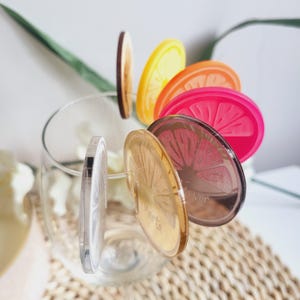 May include: A set of six colorful acrylic drink markers with a citrus fruit design. The markers are in a glass and feature the names "Marta" and "Trevor".