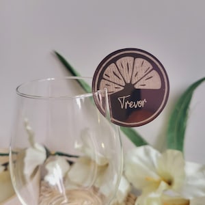 May include: Brown wooden place card with a lemon slice design and the name "Trevor" written on it.