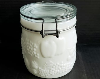 Peut inclure: Un bocal de rangement en verre opalin blanc orné d'un motif de fruits en relief représentant des raisins et des pommes. Le bocal possède un couvercle en verre transparent fixé par un mécanisme de fermeture à levier en métal.