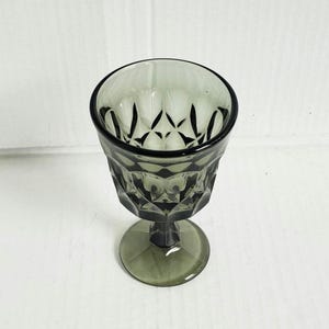 May include: A single, olive-green colored, vintage-style goblet. The glass features a diamond-patterned design on the bowl and a circular base. The stem is short and sturdy. The goblet is empty and sits on a white surface.