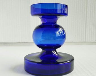 Peut inclure: Un bougeoir en verre bleu cobalt doté d'une large base circulaire, d'une section centrale sphérique et d'une ouverture supérieure cylindrique. L'objet est fabriqué en verre bleu lisse et translucide avec une finition de surface réfléchissante.