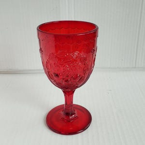 May include: A red glass goblet with a floral pattern etched into the bowl. The goblet has a stem and a round base. The glass is a deep, transparent red color. The goblet is likely used for serving beverages.