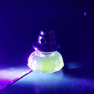 May include: A black bottle stopper with a rounded top and a light green, textured base. The stopper is illuminated with a purple light, creating a glowing effect. The product is likely for wine bottles.