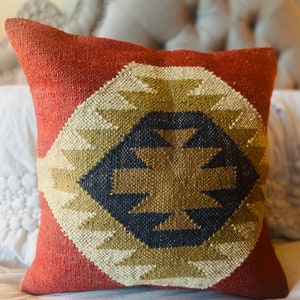 May include: Red, white, and brown geometric patterned throw pillow with a woven texture.
