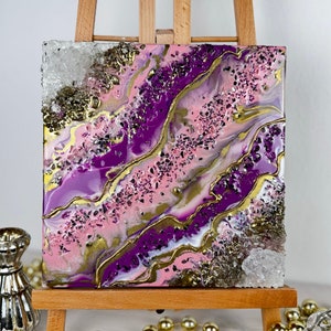Könnte beinhalten: Ein kleines quadratisches Leinwandbild mit abstrakten Wirbeln in Rosa, Lila und Gold. Das Bild ist mit kleinen weißen Kristallen bedeckt.