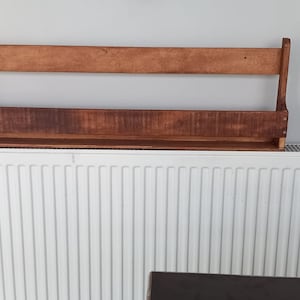 May include: A wooden shelf with two shelves is mounted on a white wall above a white radiator.