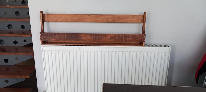 May include: A wooden shelf with two shelves is mounted on a white wall above a white radiator.