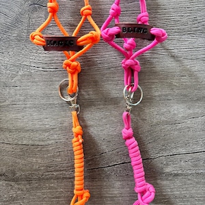 May include: Two paracord lanyards featuring neon orange and neon pink knotted cord designs. Each lanyard includes a dark brown leather tag with the words MAGIC and BLING embossed in black, a silver metal split ring, and a swivel lobster clasp.