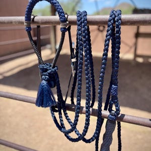 May include: A navy blue horse halter and lead rope set. The halter features a braided design with silver-toned hardware and a matching tassel. The lead rope is also navy blue and braided. The set is designed for equestrian use.