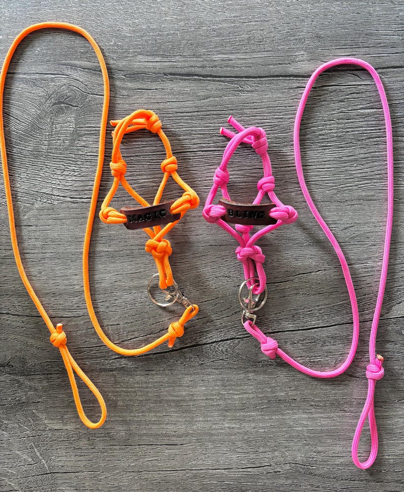 May include: Two neon-colored rope halters with long leads. The left halter is neon orange with a dark brown leather-like tag embossed with the word MAGIC. The right halter is neon pink with a dark brown leather-like tag embossed with the word BLING.