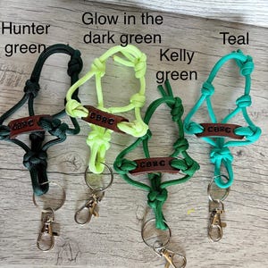 May include: Four paracord lanyards in hunter green, glow in the dark green, kelly green, and teal. Each lanyard features a brown leather tag embossed with the text CBRC, intricate knotting, a split ring, and a silver-toned metal lobster clasp.