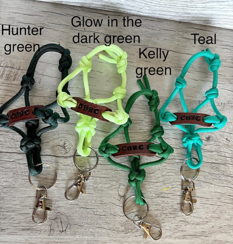 May include: Four paracord lanyards in hunter green, glow in the dark green, kelly green, and teal. Each lanyard features a brown leather tag embossed with the text CBRC, intricate knotting, a split ring, and a silver-toned metal lobster clasp.