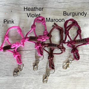 May include: Four paracord lanyards in pink, heather violet, maroon, and burgundy. Each lanyard features a knotted cord design, a brown leather tag embossed with the text CBRC, and a silver-toned metal lobster clasp attached to a split ring.