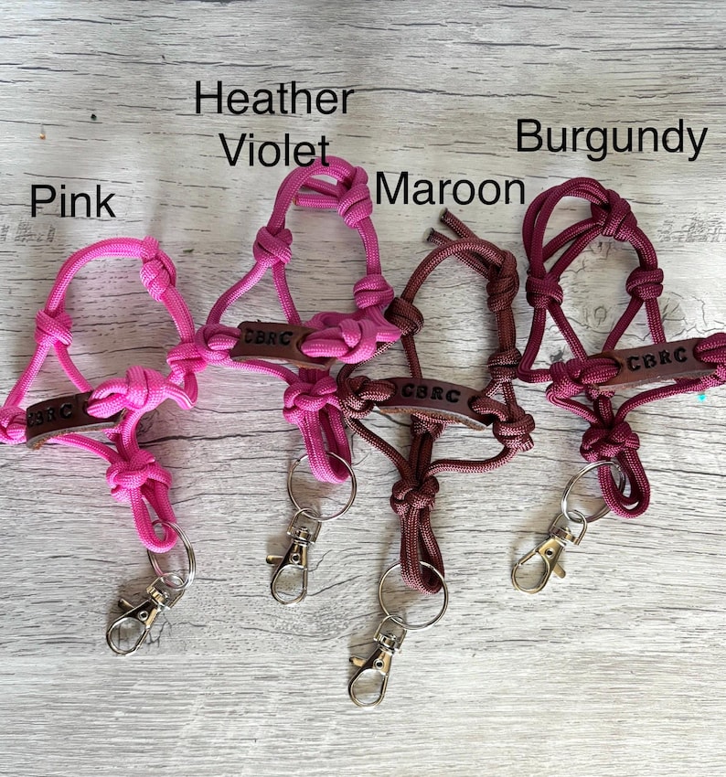 May include: Four paracord lanyards in pink, heather violet, maroon, and burgundy. Each lanyard features a knotted cord design, a brown leather tag embossed with the text CBRC, and a silver-toned metal lobster clasp attached to a split ring.