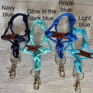 May include: Four paracord lanyards in navy blue, glow in the dark blue, royal blue, and light blue. Each lanyard features a brown leather tag embossed with the text CBRC, knotted cord construction, a metal split ring, and a silver lobster clasp.