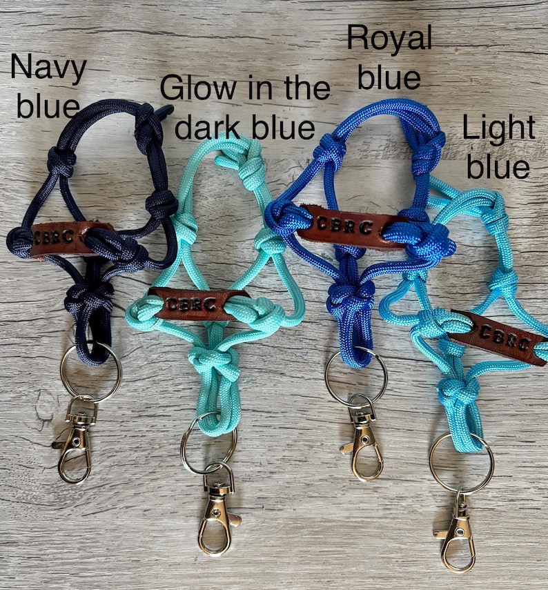 May include: Four paracord lanyards in navy blue, glow in the dark blue, royal blue, and light blue. Each lanyard features a brown leather tag embossed with the text CBRC, knotted cord construction, a metal split ring, and a silver lobster clasp.