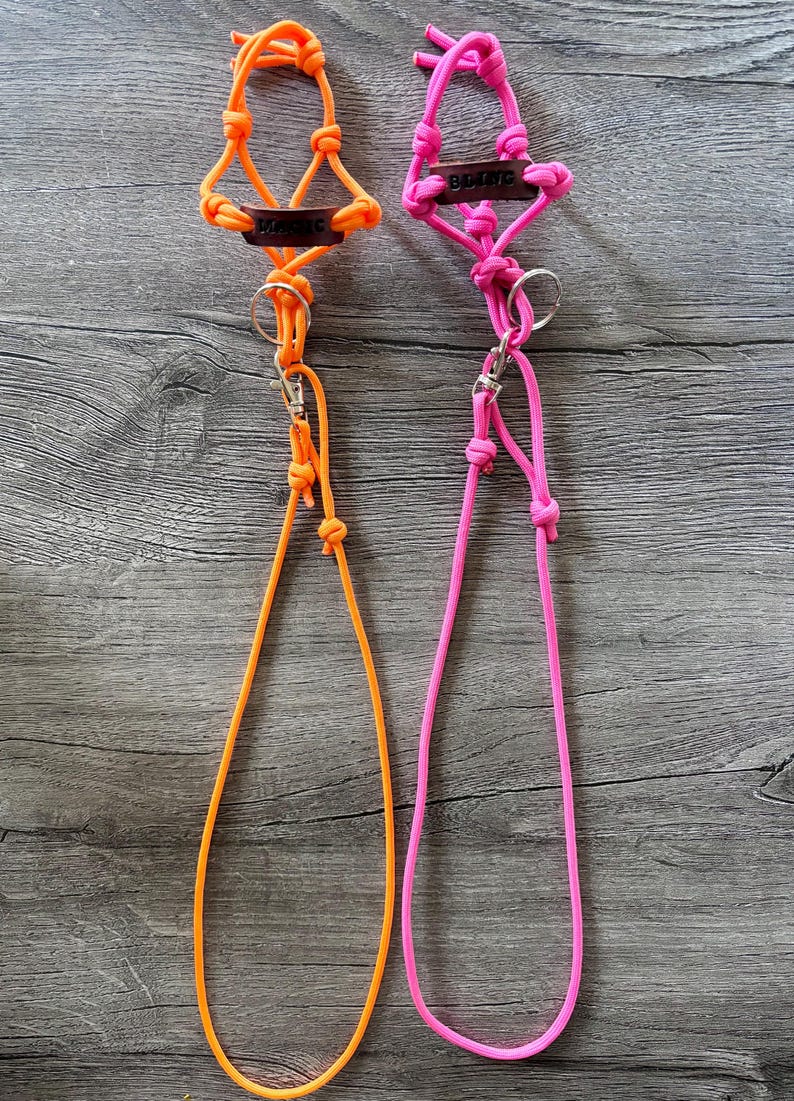 May include: Two lanyards made of neon orange and neon pink paracord, each featuring a dark brown leather tag with the word MAGIC embossed in black, a silver metal split ring, and a silver swivel lobster clasp attached to a long cord loop.