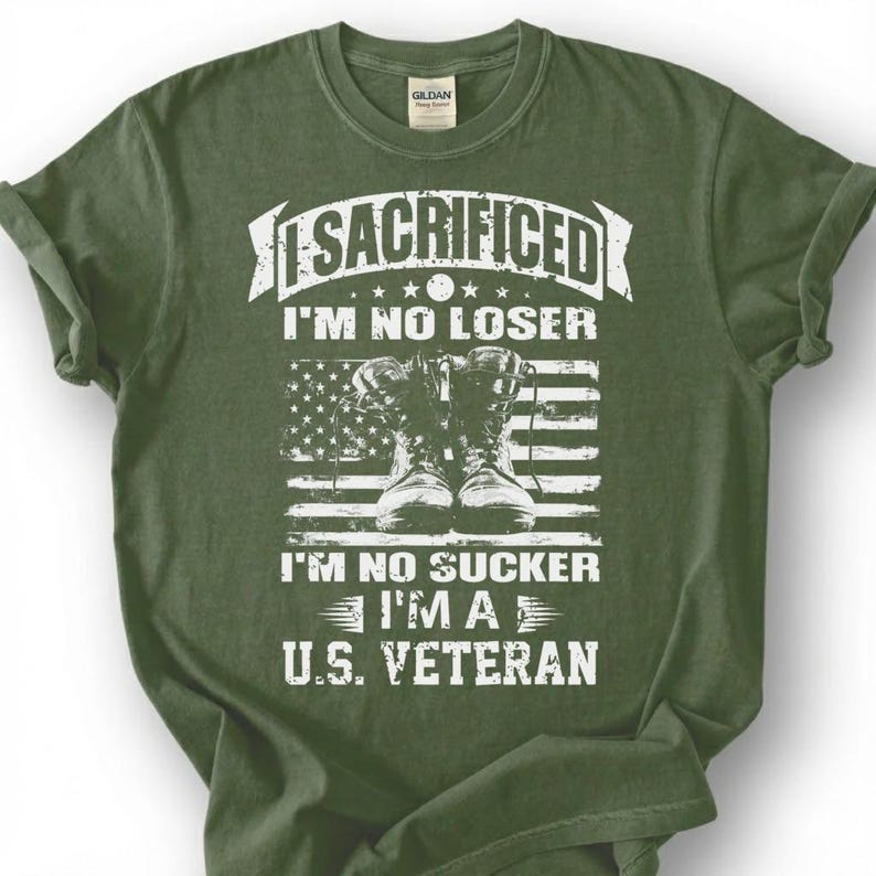 May include: Olive green t-shirt with a distressed white graphic. The graphic features combat boots in front of an American flag and the text "I SACRIFICED I'M NO LOSER I'M NO SUCKER I'M A U.S. VETERAN."