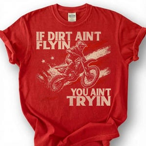 Peut inclure: T-shirt rouge avec le texte "IF DIRT AIN'T FLYIN, YOU AIN'T TRYIN" et un motard de motocross. Le design comprend un fond de style drapeau am&eacute;ricain vieilli et des &eacute;toiles.